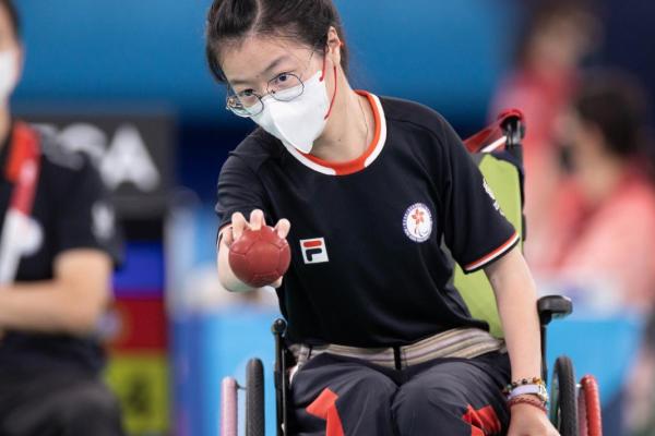 Female wheelchair boccia player aiming at target ball